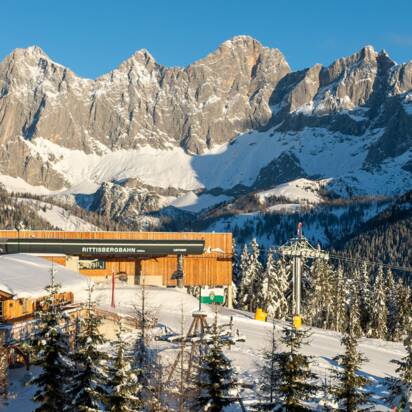 Bergstation der Rittisbergbahn mit Hütte, Spielplatz und Dachstein im Sonnenlicht.