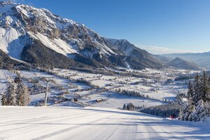 Blick von präparierter Skipiste auf verschneites Ennstal und markante Bergkulisse.