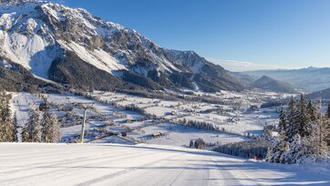 Blick von präparierter Skipiste auf verschneites Ennstal und markante Bergkulisse.