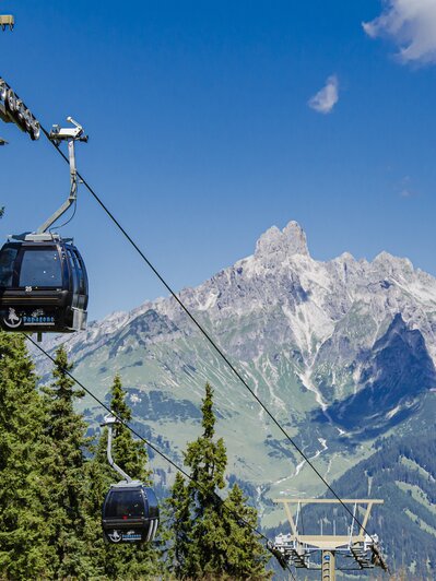 Papagenobahn cable cars schweben über Nadelwald in Filzmoos, dahinter ragt ein markantes Felsmassiv auf. | © filzmoos.ski