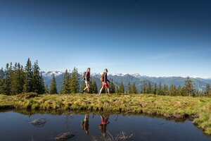 Zwei Wanderer vor spiegelndem Wasser und Alpenpanorama bei Radstadt an einem klaren Sommertag | © Salzburger Sportwelt, Lorenz Masser