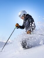 Skifahrer fährt durch den Tiefschnee und der Schnee fliegt seitlich in die Höhe