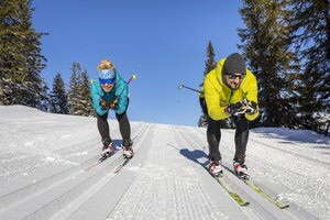 Two cross-country skiers crouching along the trail
