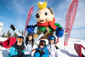 Family sits before hedgehog statue with crown standing in the snow