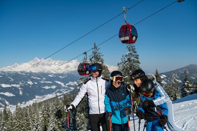Family in ski outfits laughing on slope with gondolas and alpine panorama behind