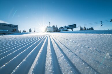 Freshly groomed ski slope with a view of the mountain lift stations from below
