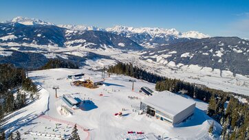 Plateau eines Skigebiets von oben mit drei Bergstationen und mehreren Skifahrern