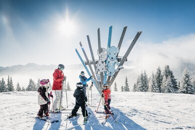 Kids with adult on skis in front of wooden sculpture with animals on Family Run at Shuttleberg resort | © Shuttleberg