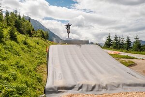 Mountain biker jumps with arms outstretched over Bagjump in green alpine setting. | © Shuttleberg