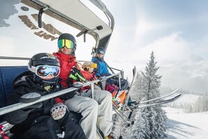 Family of four wearing ski gear on chairlift above snowy winter landscape with frosted trees | © Shuttleberg