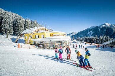 A small group of children are standing on the slope and a yellow building can be seen in the background | © Markus Rohrbacher