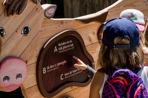 Zwei Kinder mit Kappen und Rucksack tippen auf Lernspiel in Kuhform mit Quizfrage zur Milch, Detailansicht der Station | © Snow Space Salzburg
