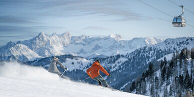 Two skiers on freshly groomed slope with gondola and Alpine panorama behind