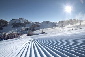 Perfectly groomed ski slopes at Alpendorf ski area with sun, snow and mountains