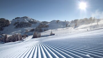 Perfectly groomed ski slopes at Alpendorf ski area with sun, snow and mountains