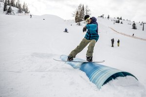Snowboarder at Betterpark Alpendorf on rail slide, snowy slope and spectators | © Gert Perauer