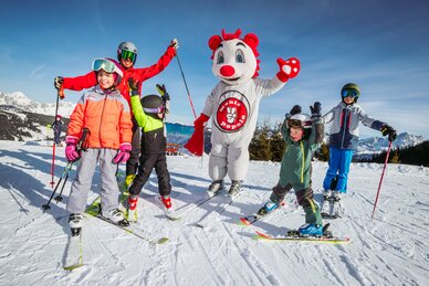 An adult and four children wave at the camera, with the Monte Popolo mascot in the middle. 