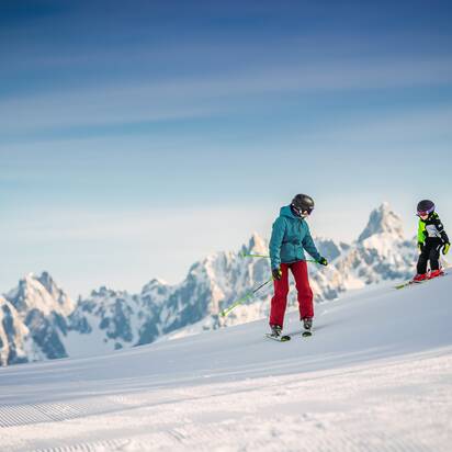 A child with rides with his dad in front of a mountain peak on freshly groomed piste. | © Snow Space Salzburg