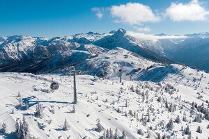 Snow-covered mountain landscape with few trees from above, over which a gondola lift runs and a ski slope can also be seen  | © Snow Space Salzburg