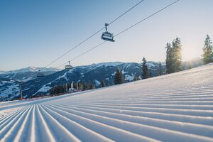 Perfectly groomed ski slope in the morning with chairlift and mountains in background | © Snow Space Salzburg