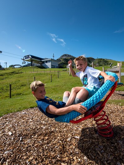 Two laughing kids swing on rope seat near Gamskogelbahn Zauchensee during summer vacation. | © Zauchensee Liftgesellschaft