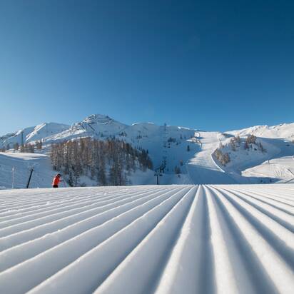 Freshly groomed piste with a view of the higher-lying piste landscape and the snow-covered surroundings