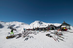 Gamskogelhütte with many skis and snowboards, people enjoying the sun, mountain panorama