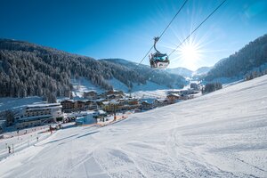 Cable car in Zauchensee valley with snowy slopes, powder snow and sun in background