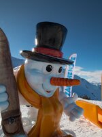 A colorful snowman with ski goggles and wooden ski, mountains and Zauchensee flags