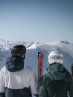 Two skiers with skis facing snowy mountains and wide panorama at Zauchensee