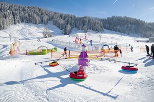 Kids in tubing carousel on snow playground with magic carpet and course in Zauchensee