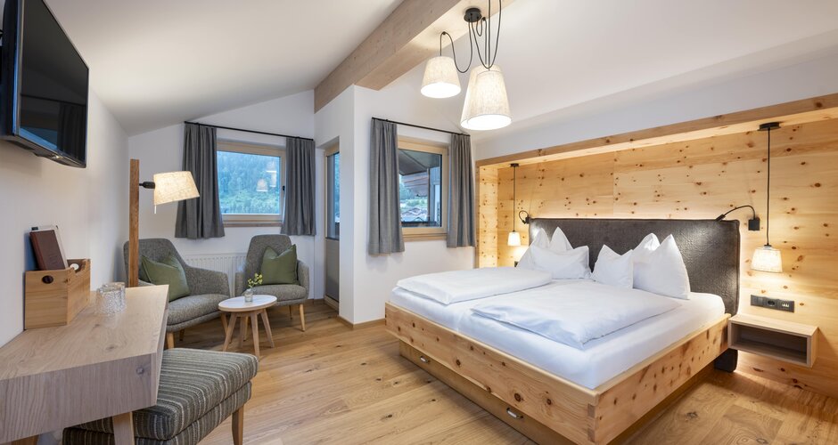 Bright double room with wooden bed, seating area, TV, desk and large windows