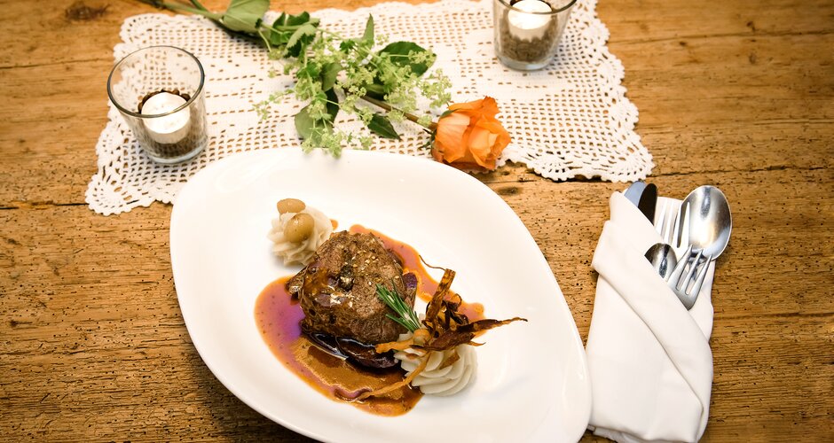 Main course with meat, sauce and purée on white plate with table decoration
