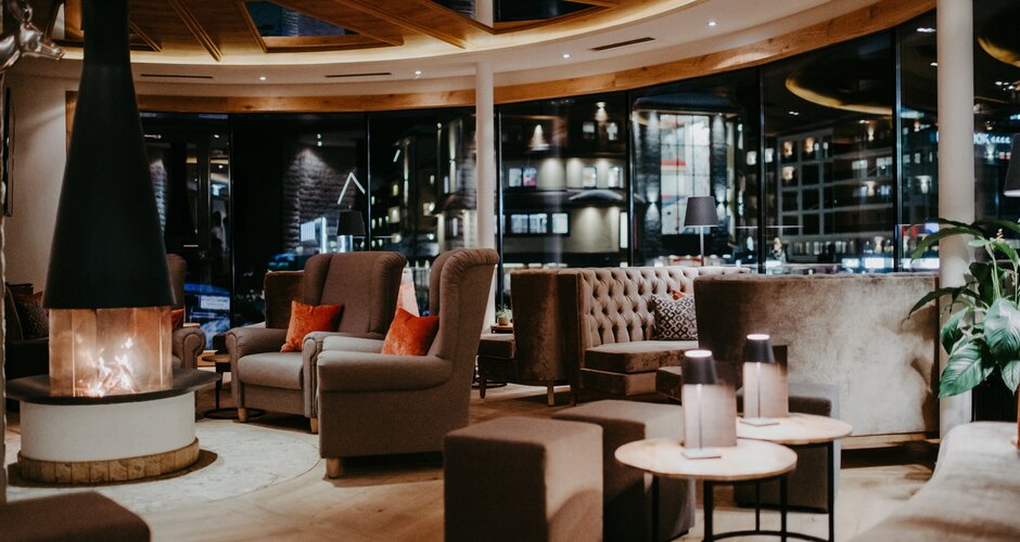 Modern hotel lounge with armchairs, sofas, tables and open fireplace at night | © Nadia Jabli