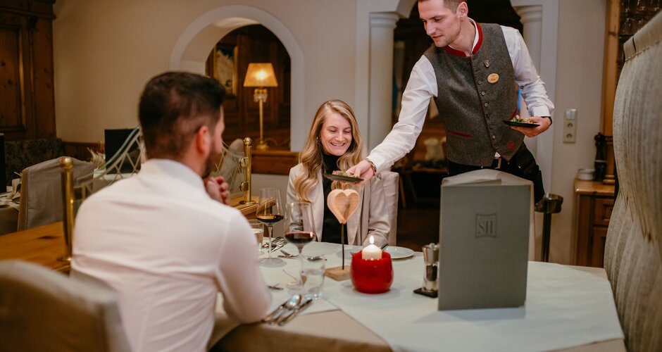 Waiter serves dinner to a couple with red wine at a festively set table | © Nadia Jabli