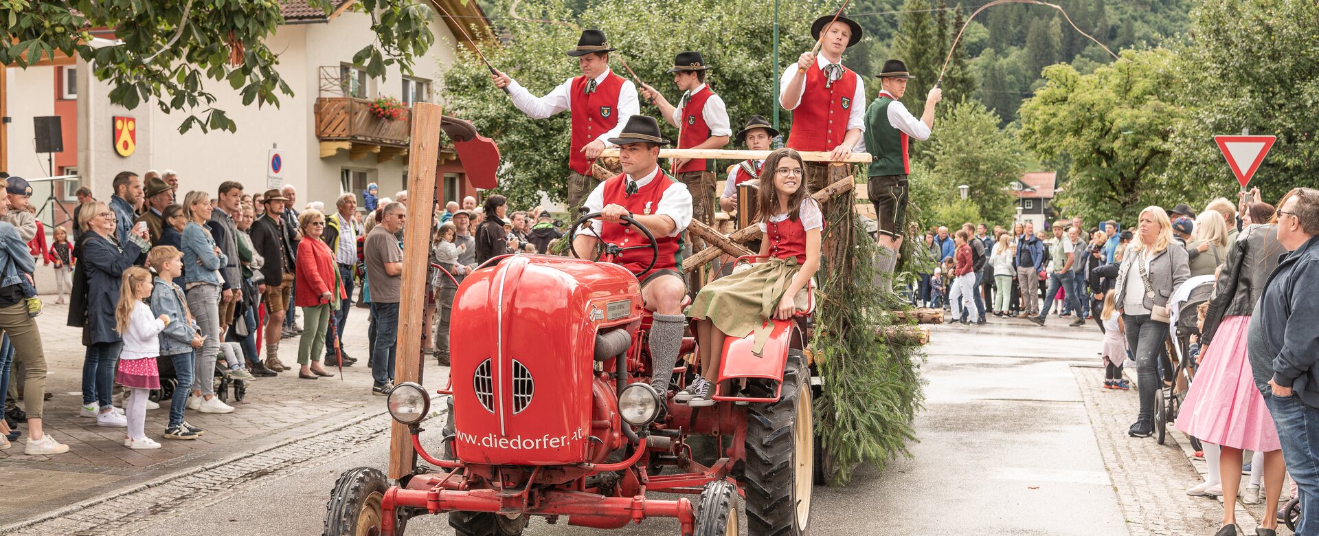 A red tractor with a trailer full of people cracking whips drives past spectators | © Gasteinertal Tourismus GmbH, Fotoatelier Wolkersdorfer