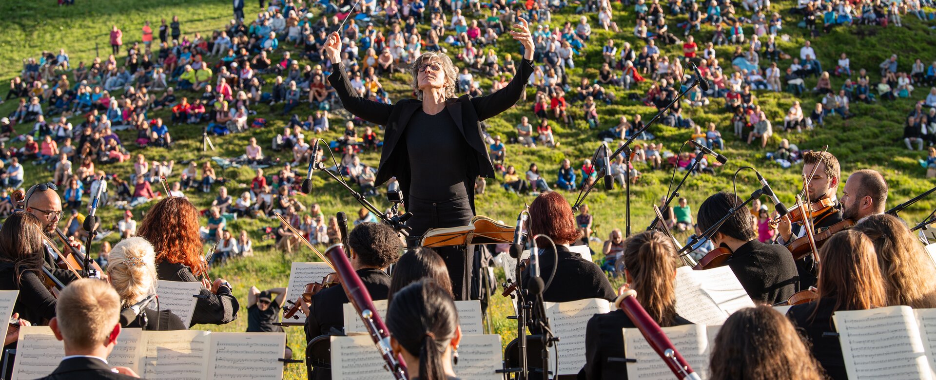 Conductor stands in front of the orchestra and behind him the audience sits on a meadow | © Gasteinertal Tourismus GmbH, Fotoatelier Wolkersdorfer 