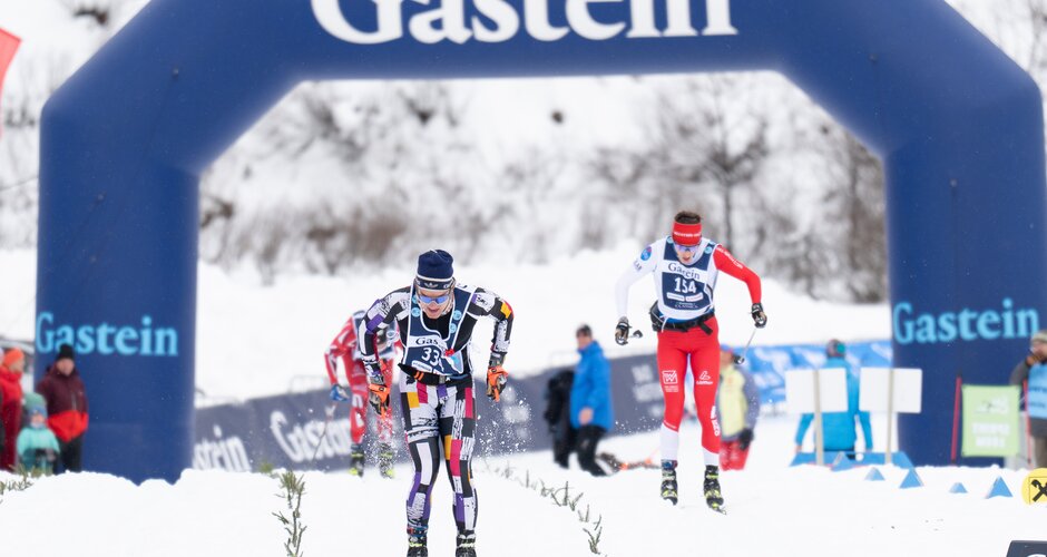Zwei Langläufer im Zielsprint unter dem Gastein-Bogen, Schneespritzer fliegen durch die Luft. | © Gasteinertal Tourismus, Mangotree Photography