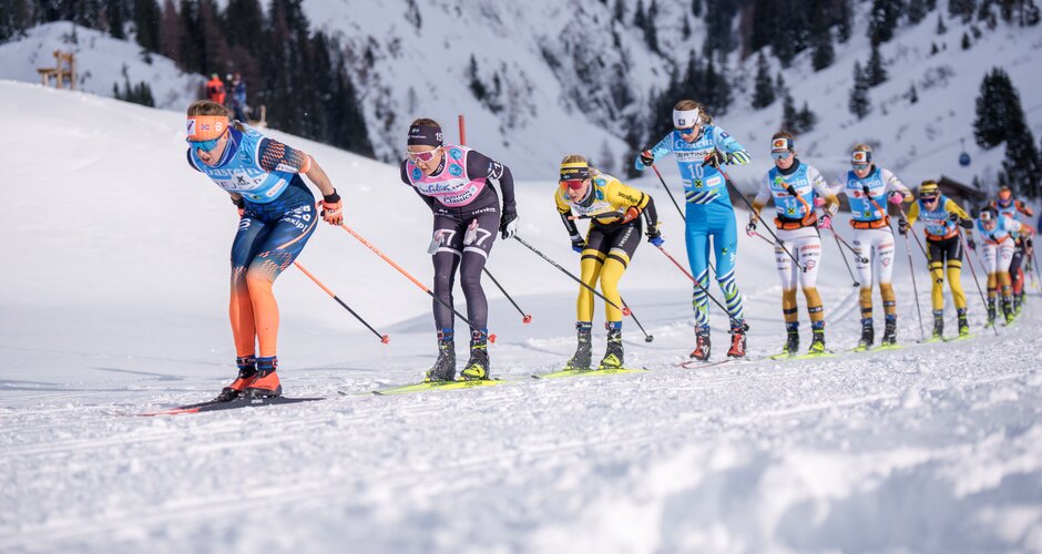 Gruppe weiblicher Langläuferinnen steigt in Rennformation bei Sonnenschein durch verschneite Berge. | © Gasteinertal Tourismus, Christoph Oberschneider