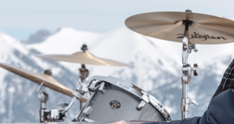 A musician plays keyboard outdoors, with drums and snowy mountain landscape in the background. | © Gasteinertal Tourismus GbmH, Marktl Photography