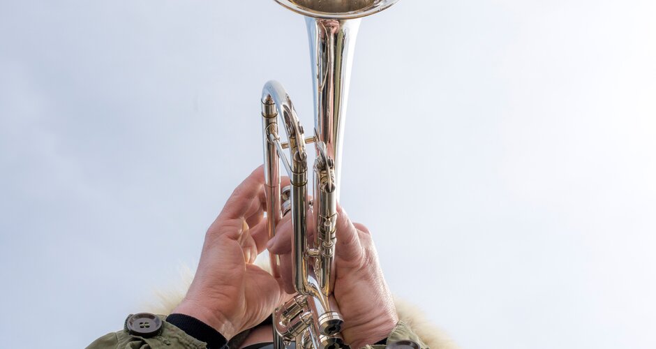 A musician plays trumpet outdoors in a parka, facing the bright winter sky above. | © Gasteinertal Tourismus GbmH, Marktl Photography