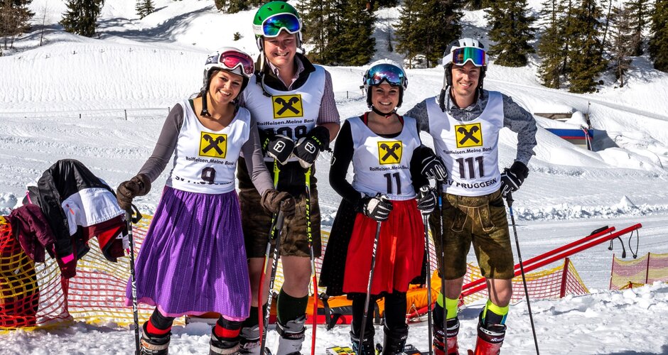 Four skiers stand on skis in traditional costume and with start numbers and smile | © David Stocker