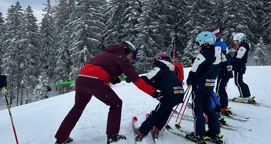 Fünf Kinder stehen nebeneinander während ein Erwachsener mit dem ersten Kind eine Gleichgewichtsübung mit den Skistöcken durchführt | © Hauser Kaibling