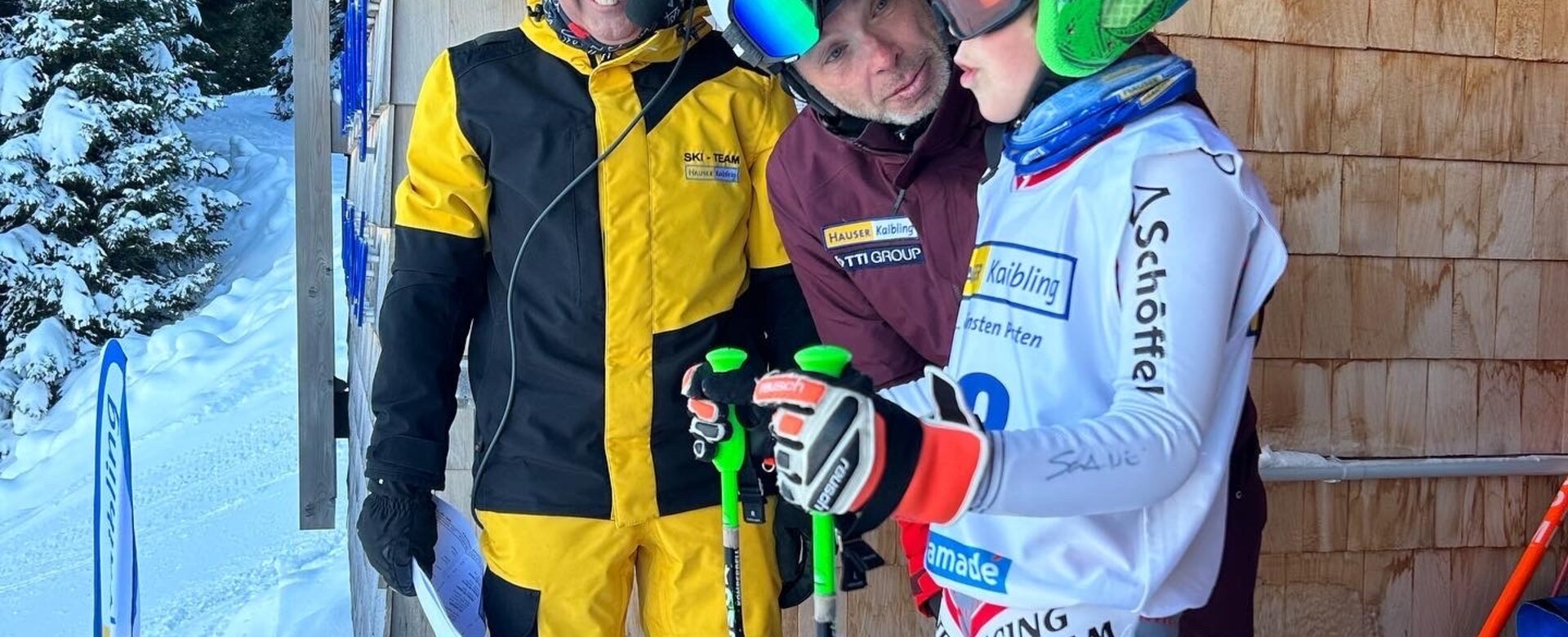 Ein Kind mit Skirennbekleidung steht in einem Starthaus während ein Erwachsener ihn ansieht und der anderen im Hintergrund in sein Headset lächelt | © Hauser Kaibling