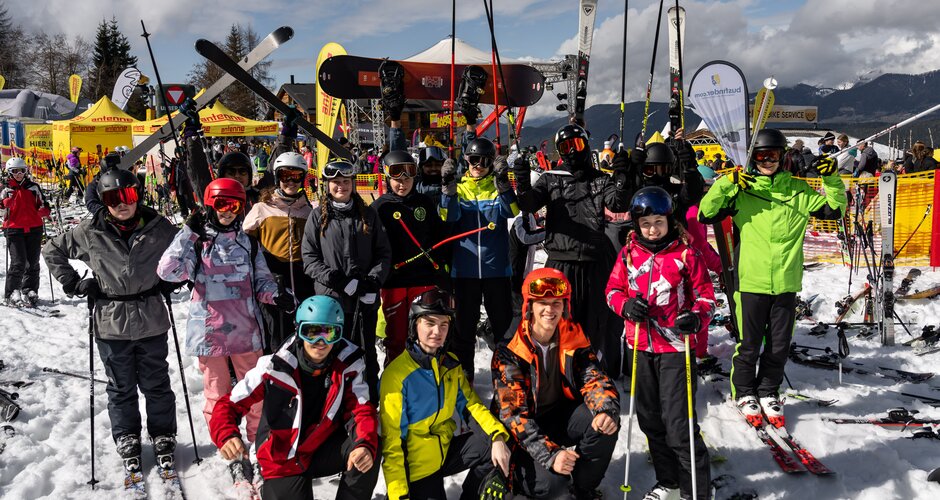Teenagers with skis and snowboards pose in snow in front of stage at Antenne Snowday. | © Ripix