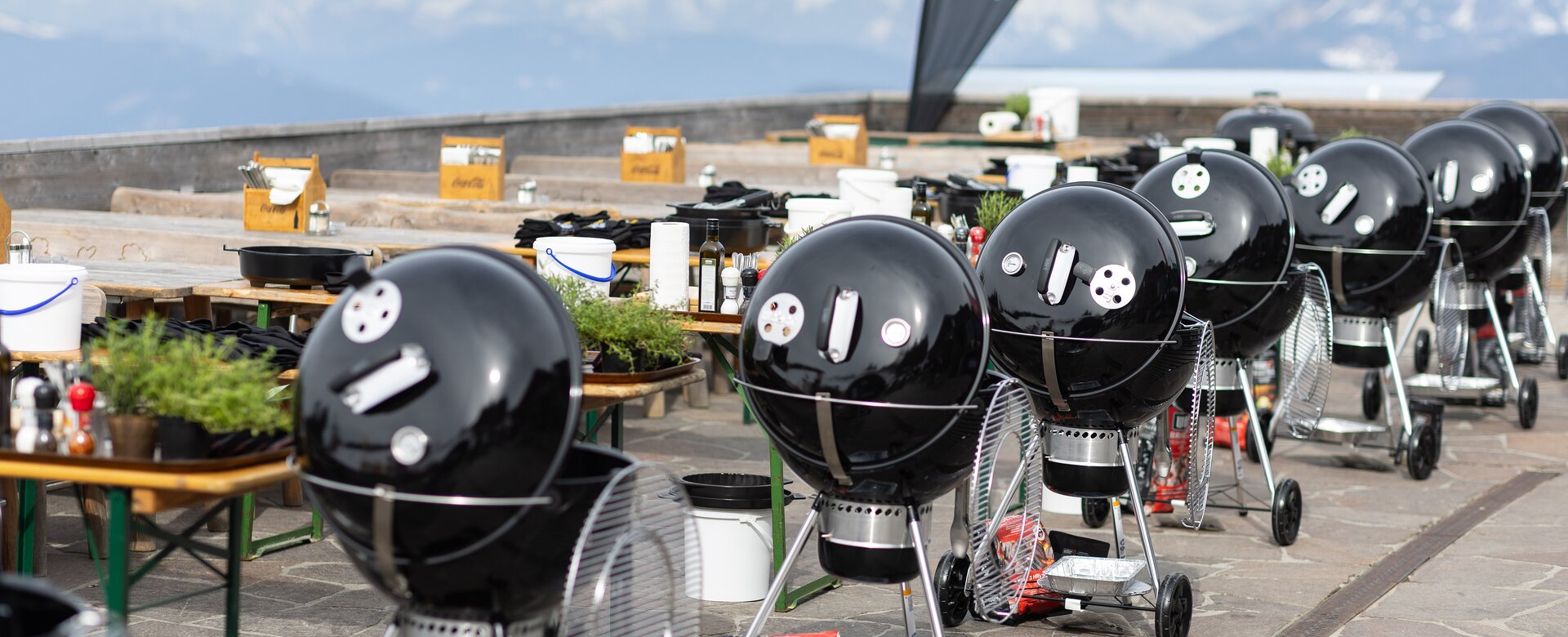Reihe schwarzer Kugelgrills mit Zubehör auf einer Terrasse mit Blick auf Bergpanorama. | © Harald Steiner