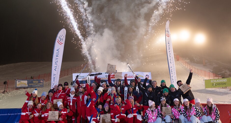 Large winning group poses in front of fireworks and banners on a night ski slope | © Michael Simonlehner