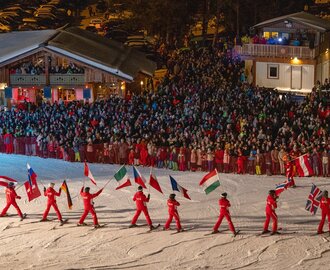 Skifahrer in Rot tragen Nationalflaggen vor großem Publikum bei Nacht auf der Piste | © Michael Simonlehner