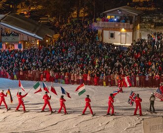 Skifahrer in Rot tragen Nationalflaggen vor großem Publikum bei Nacht auf der Piste | © Michael Simonlehner