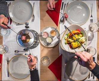 Vier Personen genießen Fleischfondue mit buntem Gemüse und Saucen an festlich gedecktem Tisch | © Martin Huber